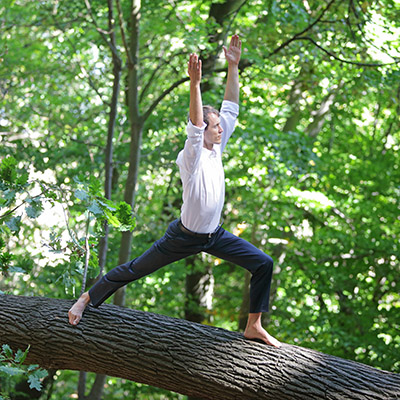Mann in Business-Outfit praktiziert Yoga auf einem Baumstamm